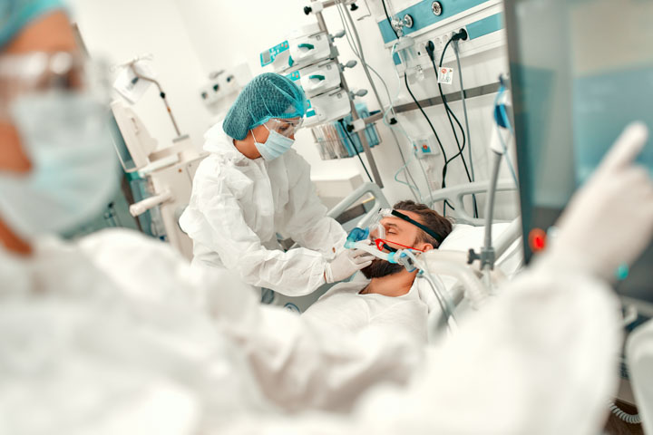 Doctors in protective suits put on a ventilation mask on a sick man with coronavirus disease covid-19, who is in an intensive care unit in a modern hospital.