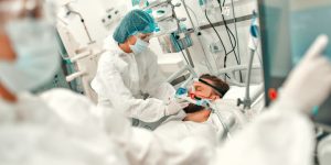 Doctors in protective suits put on a ventilation mask on a sick man with coronavirus disease covid-19, who is in an intensive care unit in a modern hospital.